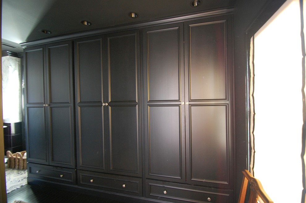 Diseño de armario vestidor unisex contemporáneo con armarios con paneles empotrados, puertas de armario negras y suelo de madera oscura