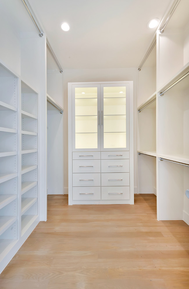 Ejemplo de armario vestidor unisex actual grande con armarios con paneles lisos, puertas de armario blancas y suelo de madera clara