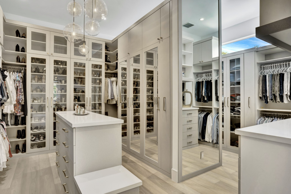 Large contemporary gender neutral walk-in wardrobe in Miami with glass-front cabinets, grey cabinets, light hardwood flooring and beige floors.