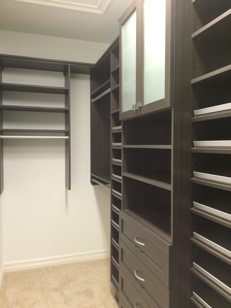 Large modern gender neutral walk-in wardrobe in Miami with shaker cabinets, dark wood cabinets, carpet and beige floors.