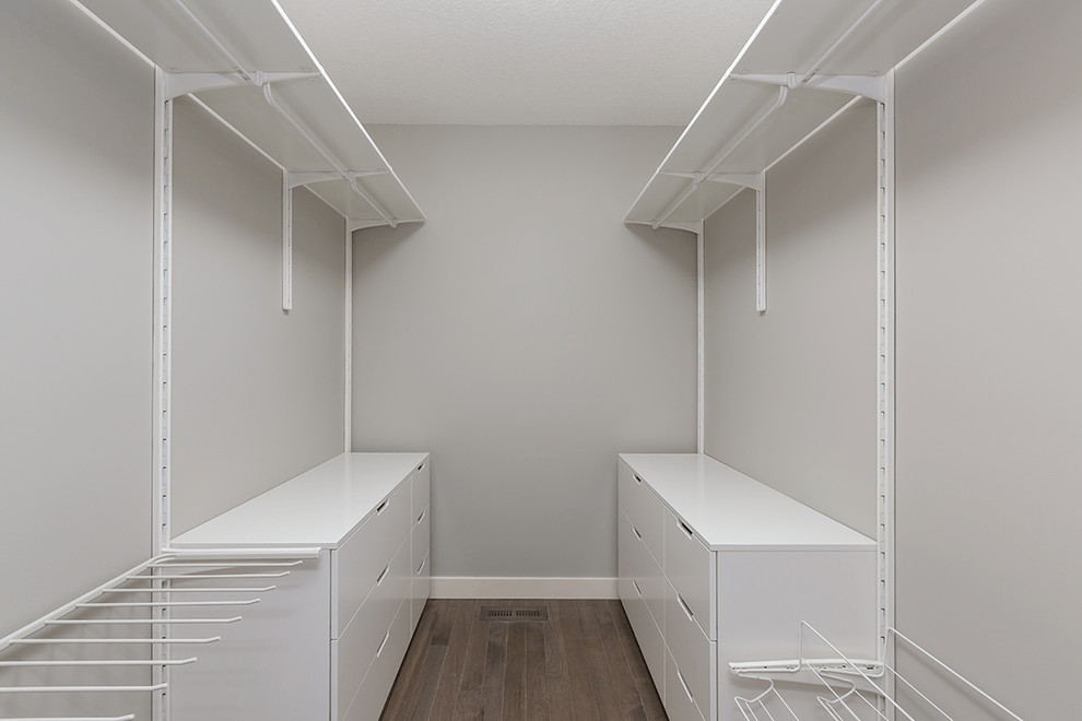 Стильный дизайн: гардеробная комната среднего размера, унисекс в современном стиле с плоскими фасадами, белыми фасадами, полом из ламината и коричневым полом - последний тренд