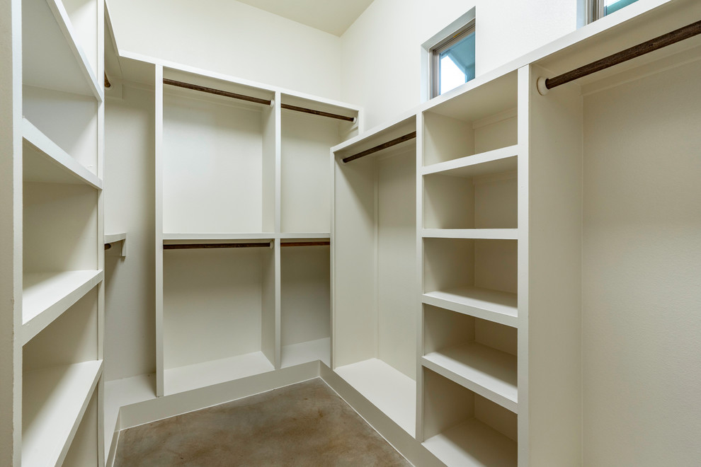 Klassisk inredning av ett stort walk-in-closet för könsneutrala, med öppna hyllor, vita skåp, betonggolv och brunt golv