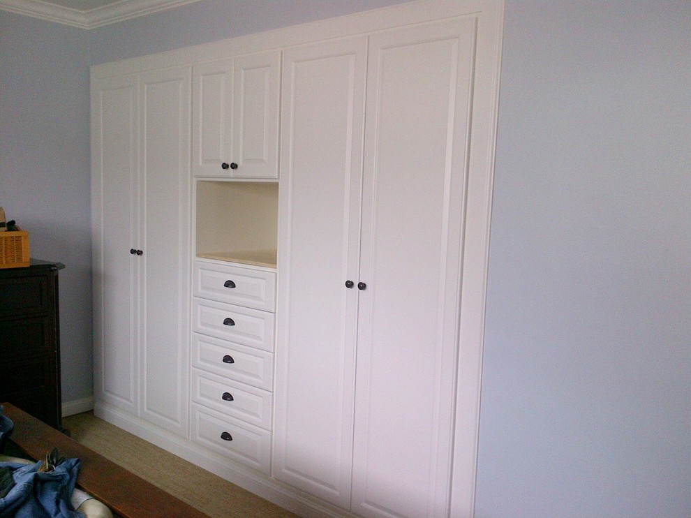 Foto de armario unisex clásico pequeño con armarios con paneles con relieve, puertas de armario blancas y suelo de madera clara