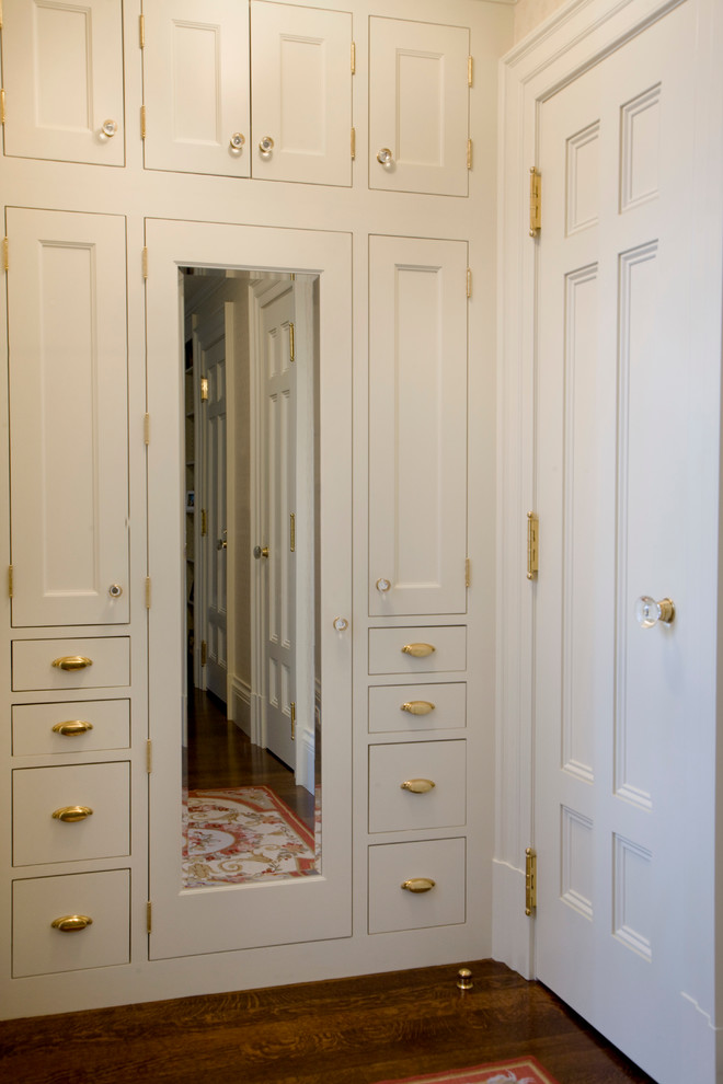 Diseño de armario y vestidor unisex clásico pequeño con armarios con paneles empotrados, puertas de armario blancas y suelo de madera oscura