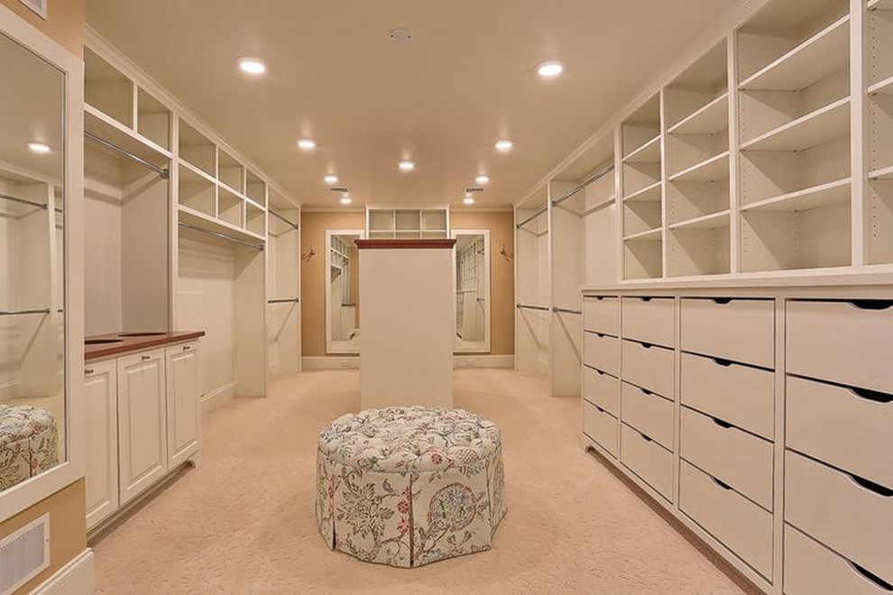 Photo of a large classic gender neutral walk-in wardrobe in Other with flat-panel cabinets, white cabinets, carpet and beige floors.
