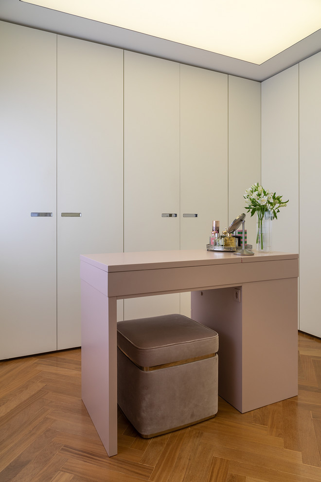 Photo of a contemporary dressing room for women in Other with flat-panel cabinets, white cabinets and medium hardwood flooring.
