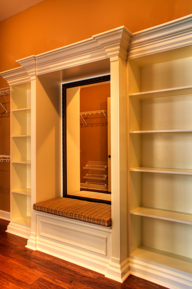 Diseño de armario vestidor unisex clásico con armarios con paneles con relieve, puertas de armario blancas y suelo de madera en tonos medios