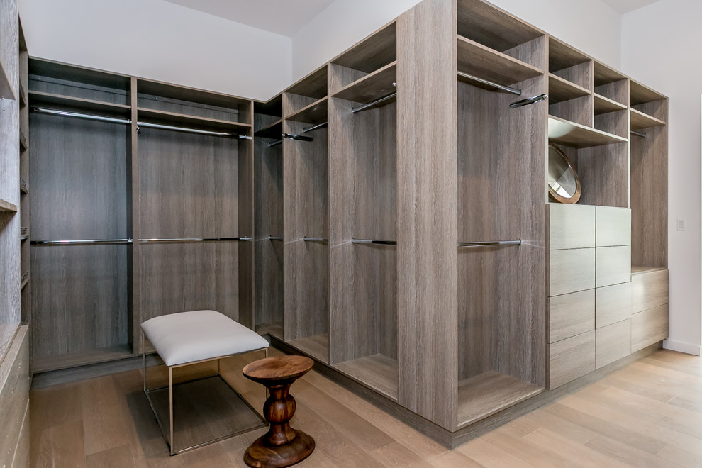 Diseño de armario vestidor unisex actual extra grande con armarios con paneles lisos, puertas de armario grises y suelo de madera en tonos medios
