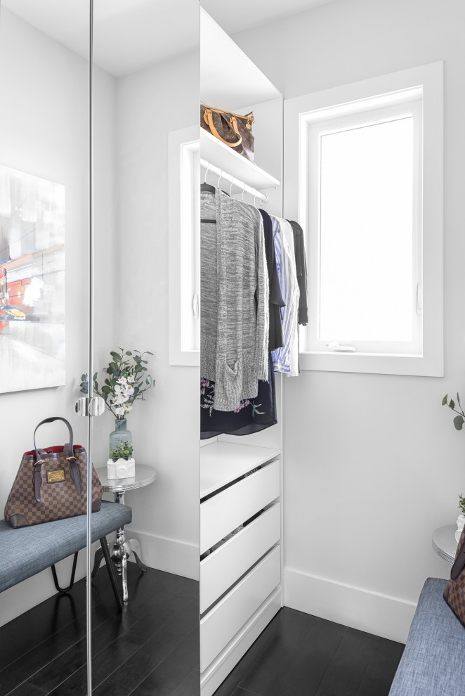 Modelo de armario vestidor de mujer actual de tamaño medio con armarios con paneles lisos, puertas de armario blancas, suelo de madera oscura y suelo negro
