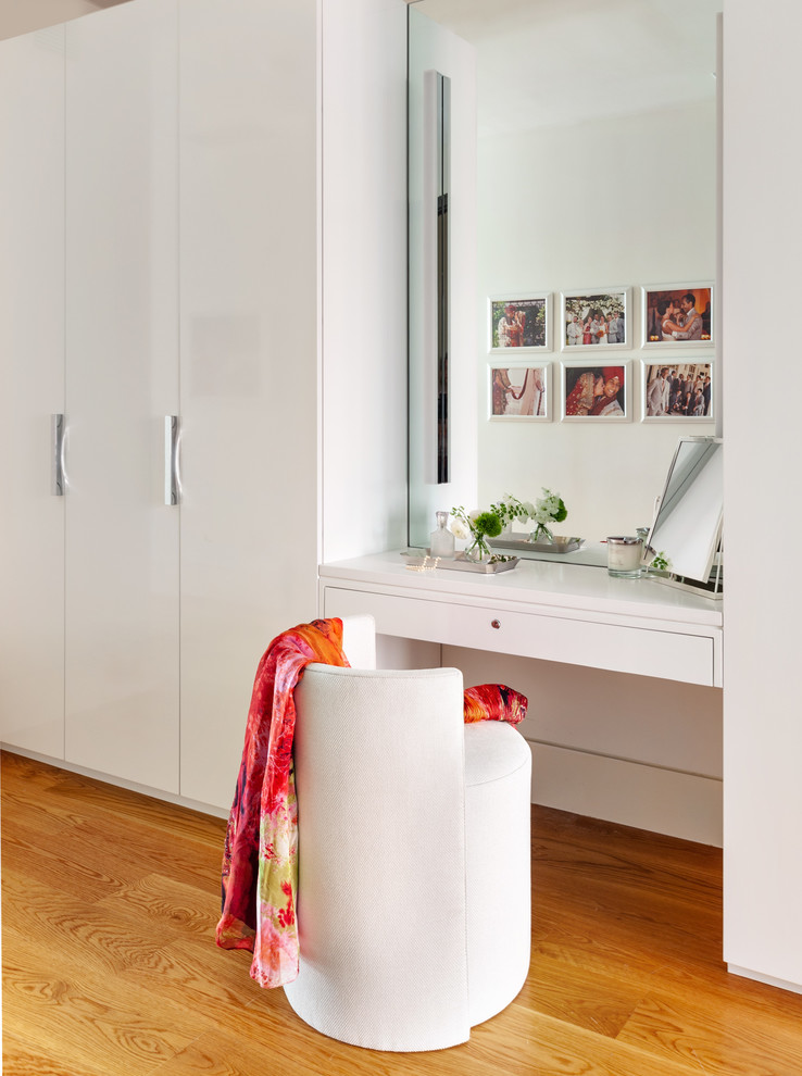Skandinavisches Ankleidezimmer mit Ankleidebereich, flächenbündigen Schrankfronten, weißen Schränken und braunem Holzboden in New York