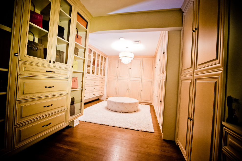 Ejemplo de armario vestidor de mujer clásico grande con armarios con paneles con relieve, puertas de armario beige, suelo de madera en tonos medios y suelo marrón