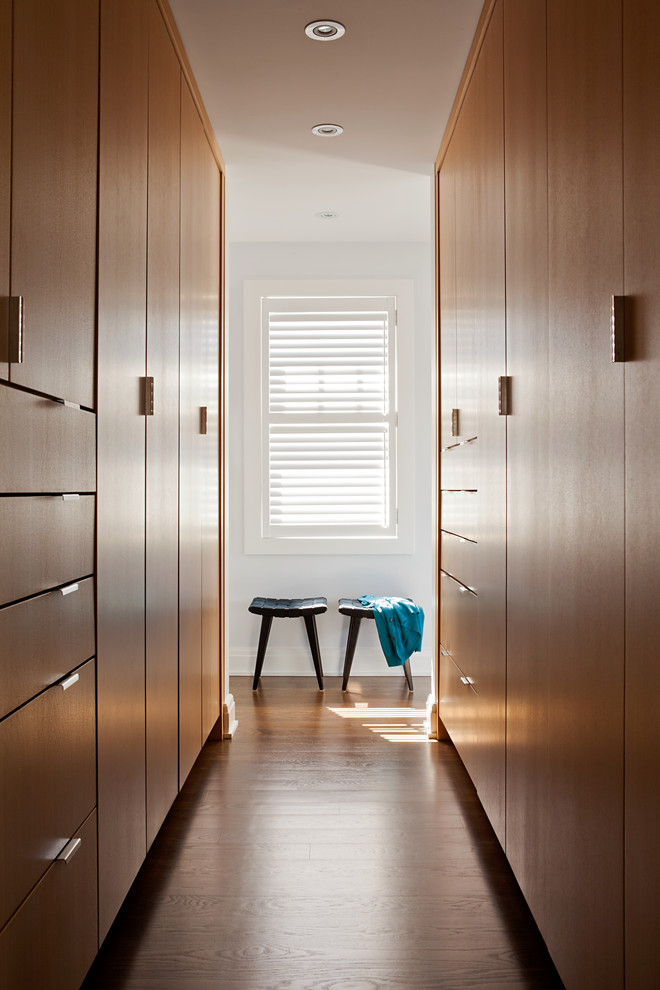 На фото: гардеробная комната унисекс в современном стиле с плоскими фасадами, фасадами цвета дерева среднего тона и паркетным полом среднего тона