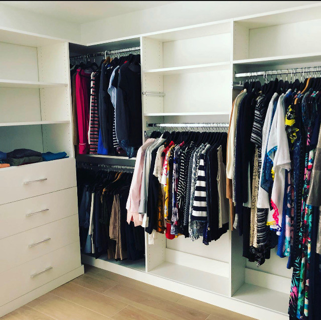 Example of a mid-sized trendy women's laminate floor and brown floor walk-in closet design in Miami with flat-panel cabinets and white cabinets