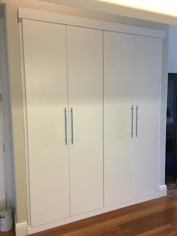 Diseño de armario de hombre contemporáneo pequeño con armarios con paneles lisos, puertas de armario blancas y suelo de madera en tonos medios