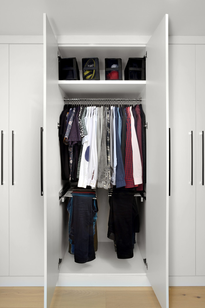Imagen de armario unisex actual de tamaño medio con armarios con paneles lisos, puertas de armario blancas, suelo de madera clara y suelo beige