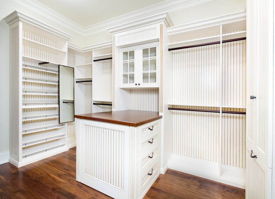 Diseño de armario vestidor unisex de estilo de casa de campo grande con puertas de armario blancas, suelo de madera en tonos medios y armarios con paneles empotrados