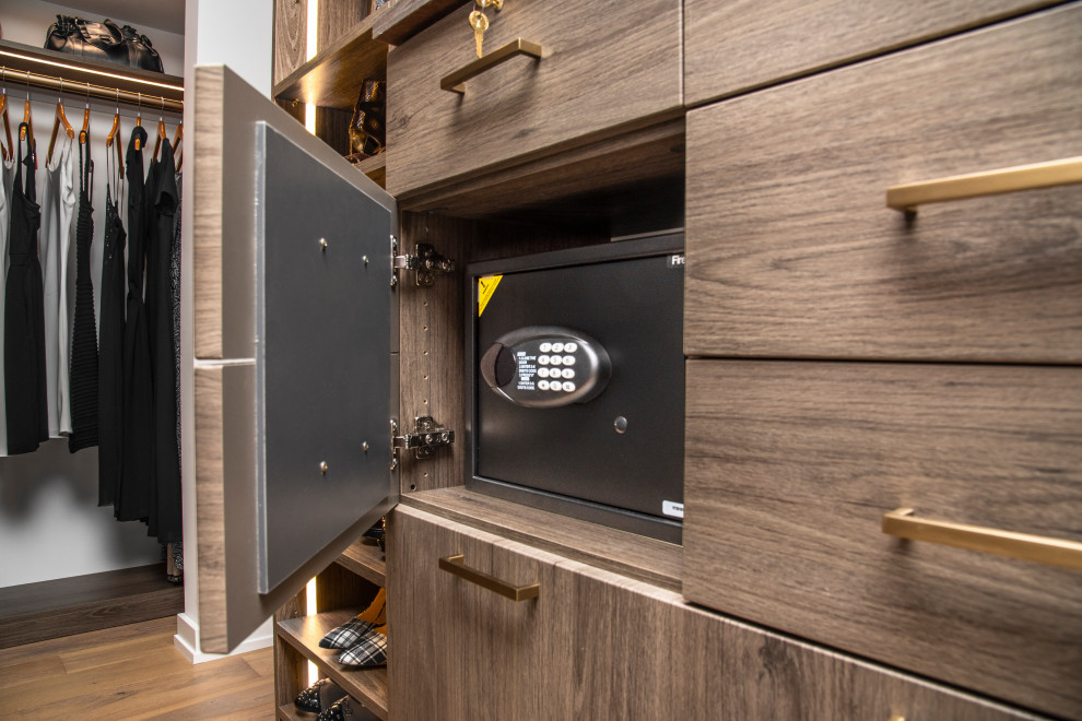 Ejemplo de armario vestidor unisex actual grande con armarios con paneles lisos, puertas de armario de madera oscura, suelo de madera clara y suelo beige