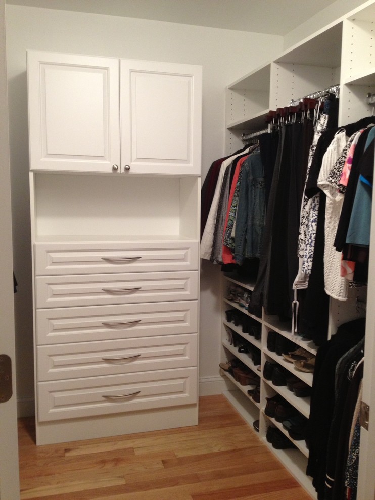 Imagen de armario vestidor unisex clásico de tamaño medio con armarios abiertos, puertas de armario blancas y suelo de madera clara