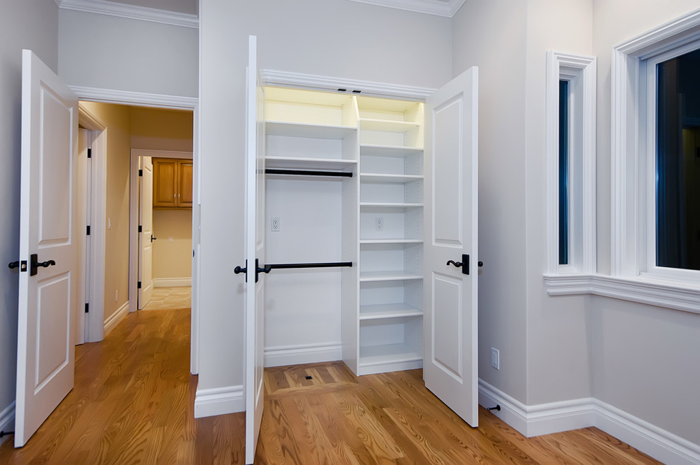Modelo de armario unisex tradicional de tamaño medio con armarios abiertos, puertas de armario blancas, suelo de madera en tonos medios y suelo marrón