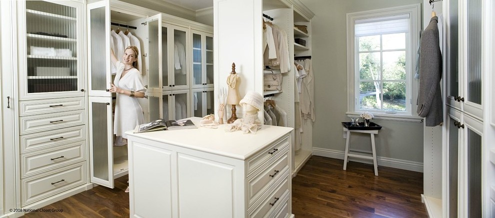 Modelo de vestidor unisex clásico grande con armarios con paneles con relieve, puertas de armario blancas, suelo de madera oscura y suelo marrón
