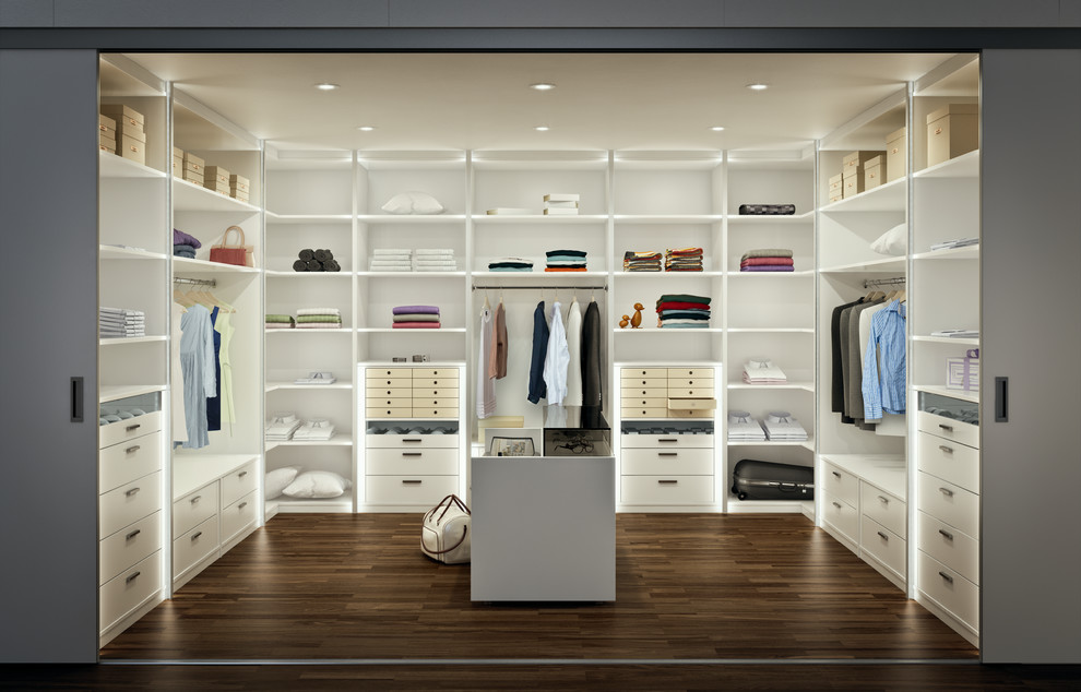 Diseño de armario vestidor unisex actual grande con armarios con paneles lisos, puertas de armario blancas y suelo de madera oscura