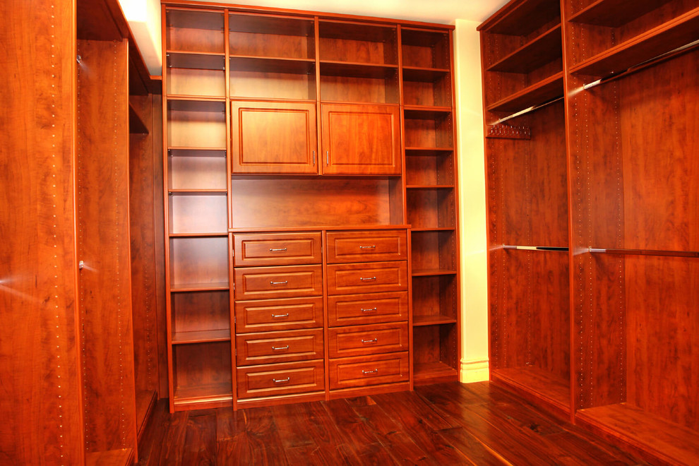 Modelo de armario vestidor unisex tradicional renovado grande con armarios con paneles con relieve, suelo de madera en tonos medios y puertas de armario de madera oscura