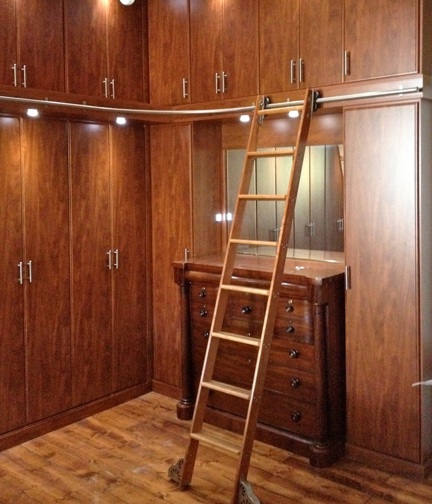 Imagen de armario vestidor unisex clásico de tamaño medio con armarios con paneles lisos, puertas de armario de madera oscura y suelo de madera en tonos medios