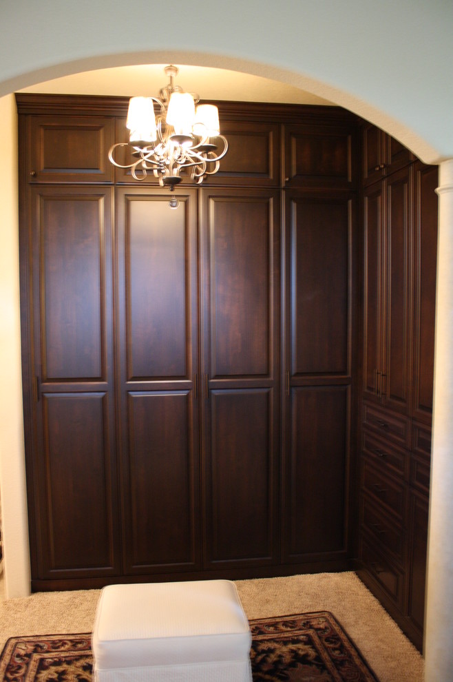 Example of a mid-sized classic gender-neutral carpeted walk-in closet design in Sacramento with raised-panel cabinets and dark wood cabinets
