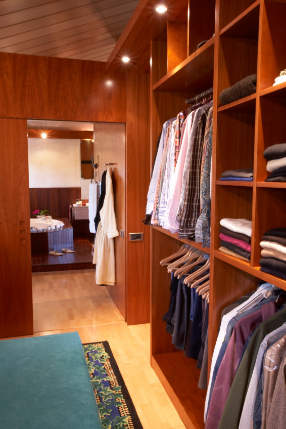 Ejemplo de armario vestidor unisex actual de tamaño medio con armarios con paneles lisos, puertas de armario de madera oscura y suelo de madera clara