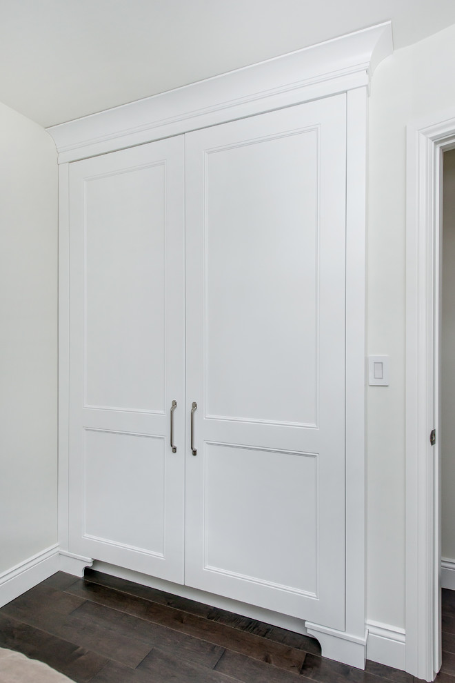 Modelo de armario unisex clásico renovado de tamaño medio con armarios con paneles empotrados, puertas de armario blancas y suelo de madera oscura