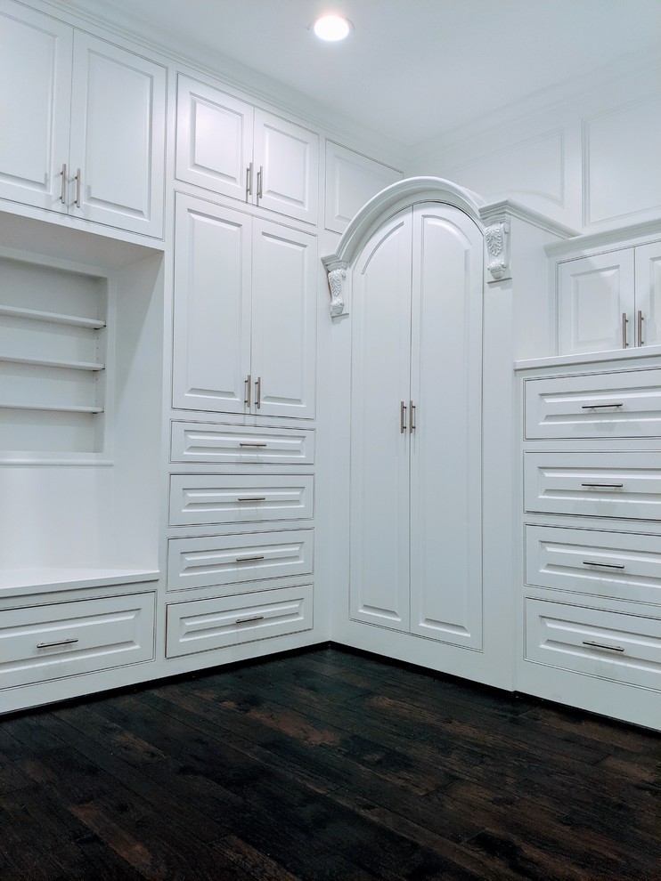 Modelo de armario vestidor unisex y abovedado minimalista grande con armarios con paneles con relieve, puertas de armario blancas, suelo de madera oscura y suelo marrón