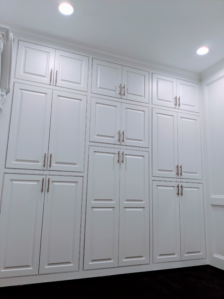 Diseño de armario vestidor unisex y abovedado minimalista grande con armarios con paneles con relieve, puertas de armario blancas, suelo de madera oscura y suelo marrón