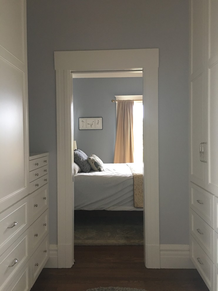 Cette photo montre un dressing chic neutre avec un placard avec porte à panneau encastré, des portes de placard blanches, parquet foncé et un sol marron.