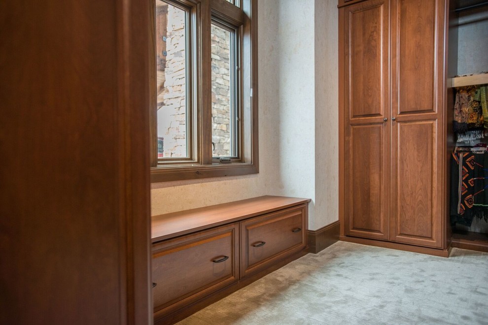 Imagen de armario vestidor unisex clásico de tamaño medio con armarios con paneles con relieve, puertas de armario de madera oscura, moqueta y suelo beige