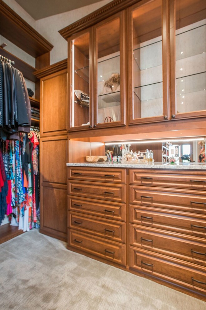 Ejemplo de armario vestidor unisex clásico de tamaño medio con armarios con paneles con relieve, puertas de armario de madera oscura, moqueta y suelo beige