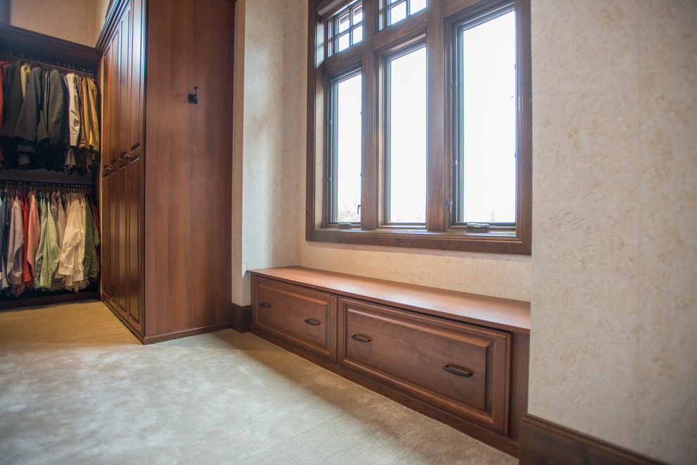 Diseño de armario vestidor unisex tradicional extra grande con armarios con paneles con relieve, puertas de armario de madera oscura, moqueta y suelo beige