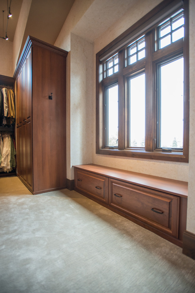 На фото: огромная гардеробная комната унисекс в классическом стиле с фасадами с выступающей филенкой, фасадами цвета дерева среднего тона, ковровым покрытием и бежевым полом