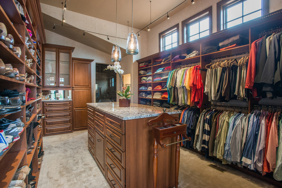 This is an example of an expansive traditional gender neutral walk-in wardrobe in Denver with raised-panel cabinets, medium wood cabinets, carpet and beige floors.