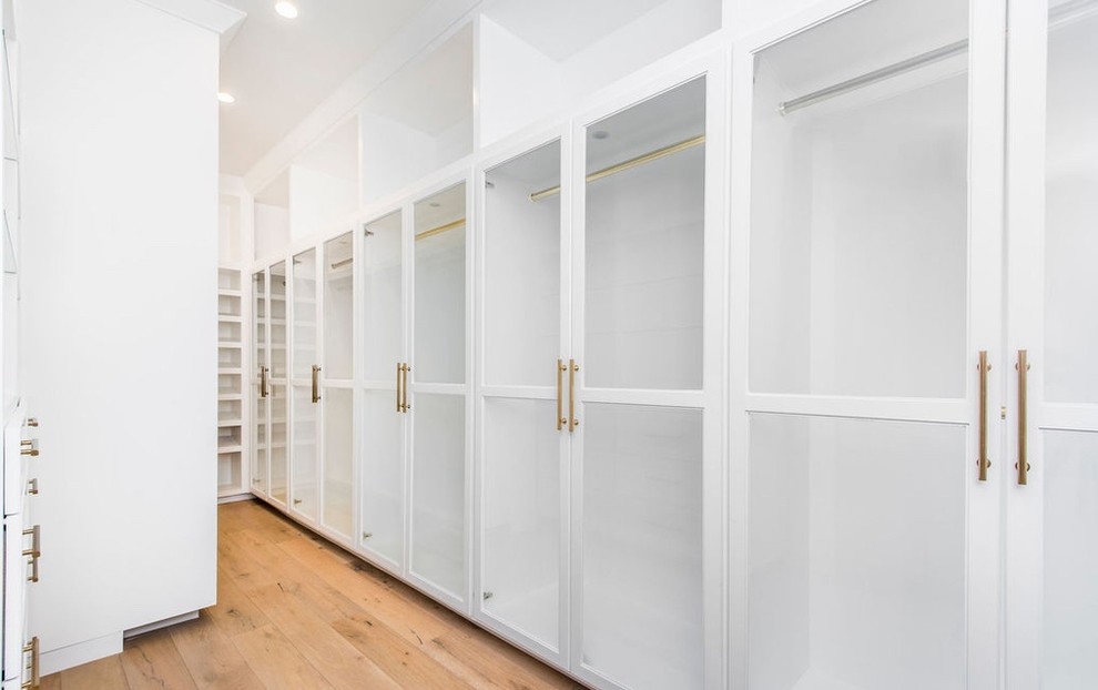 Inspiration for a large contemporary gender-neutral light wood floor and beige floor walk-in closet remodel in Los Angeles with glass-front cabinets and white cabinets