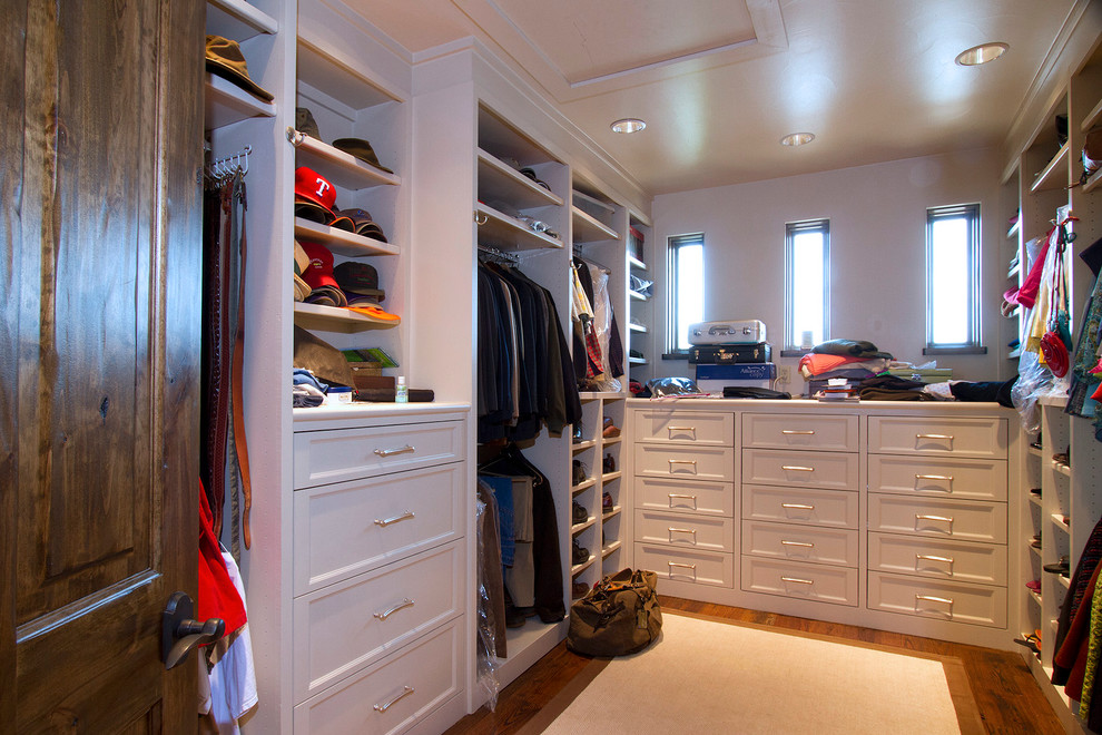 Ejemplo de vestidor unisex de estilo americano grande con armarios con paneles empotrados, puertas de armario blancas y suelo de madera clara