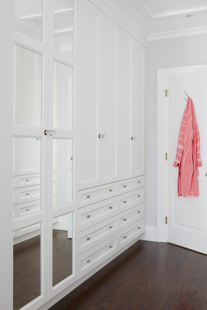 Imagen de armario vestidor unisex clásico de tamaño medio con armarios con paneles empotrados, puertas de armario blancas, suelo de madera oscura y suelo marrón