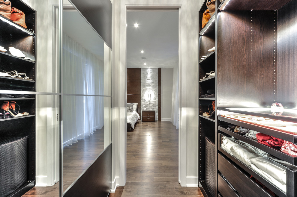 Inspiration for a medium sized contemporary gender neutral walk-in wardrobe in Montreal with glass-front cabinets, brown cabinets and medium hardwood flooring.