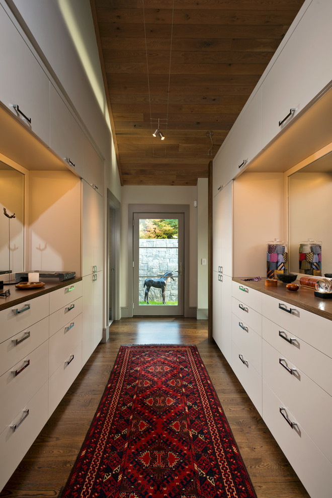 Idée de décoration pour un dressing design avec un placard à porte plane, des portes de placard blanches et un sol en bois brun.