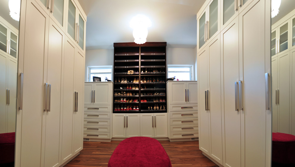 Ejemplo de vestidor unisex actual extra grande con armarios tipo vitrina, puertas de armario blancas y suelo de madera en tonos medios