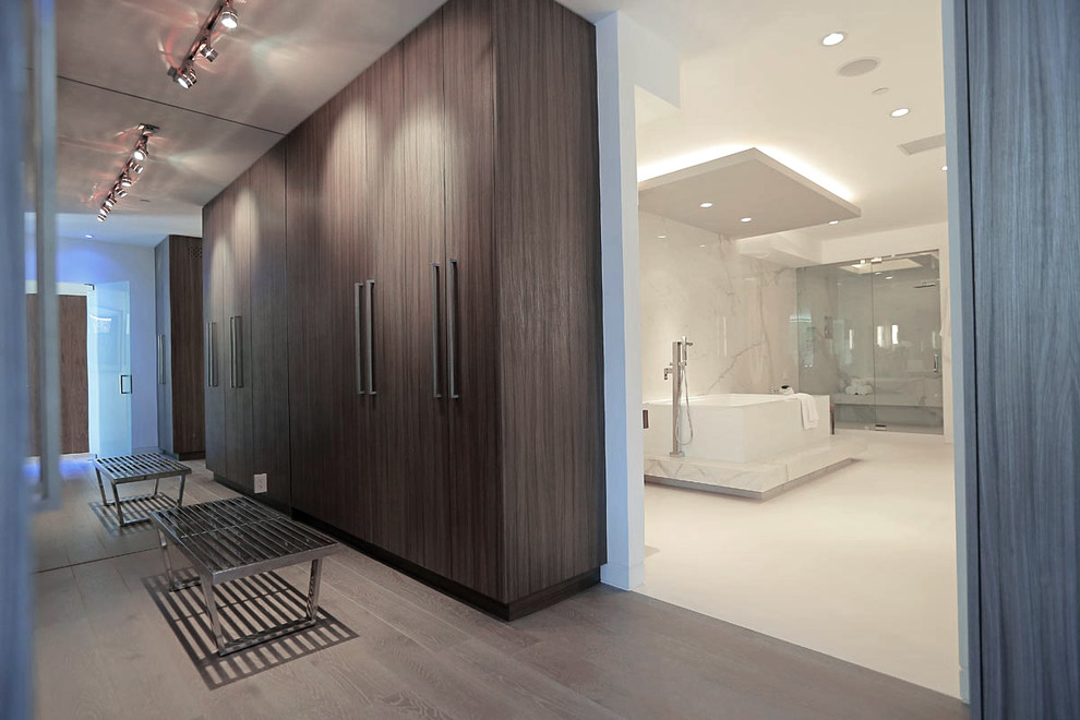 Großes, Neutrales Modernes Ankleidezimmer mit flächenbündigen Schrankfronten, hellbraunen Holzschränken, hellem Holzboden, Ankleidebereich und grauem Boden in Los Angeles
