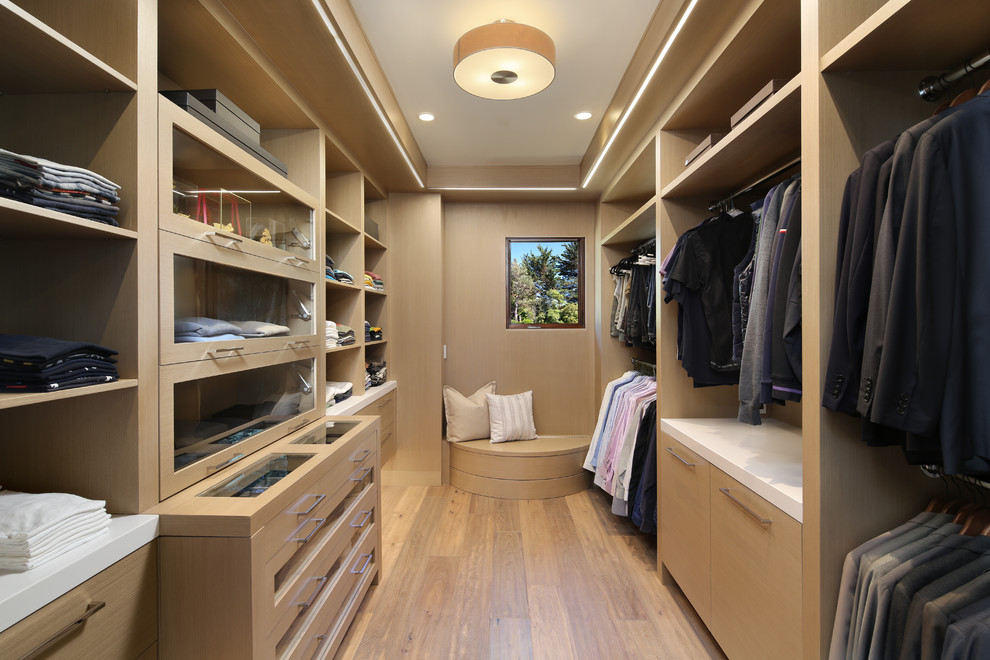 Expansive contemporary dressing room for men in San Francisco with light hardwood flooring, glass-front cabinets, beige cabinets, beige floors and feature lighting.