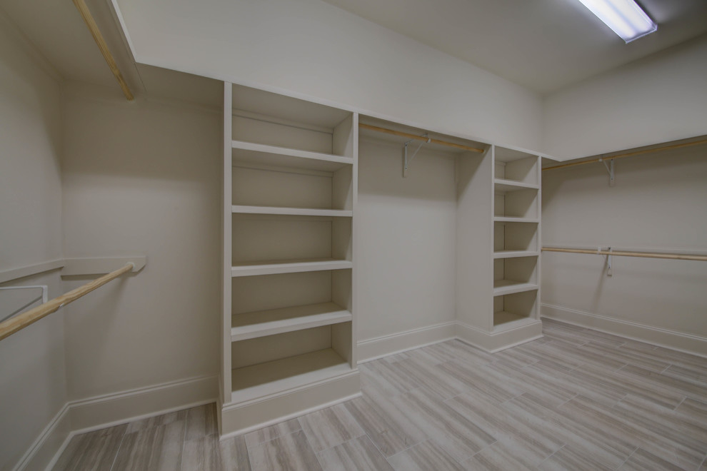 Large traditional gender neutral walk-in wardrobe in New Orleans with open cabinets, beige cabinets and porcelain flooring.
