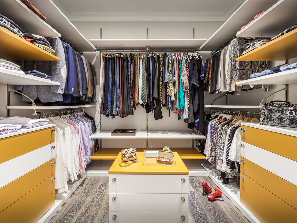 Ejemplo de armario vestidor unisex actual grande con armarios con paneles lisos, puertas de armario blancas y suelo de madera en tonos medios