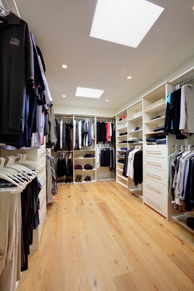 Modelo de armario vestidor unisex actual grande con armarios con paneles lisos, puertas de armario blancas y suelo de madera clara