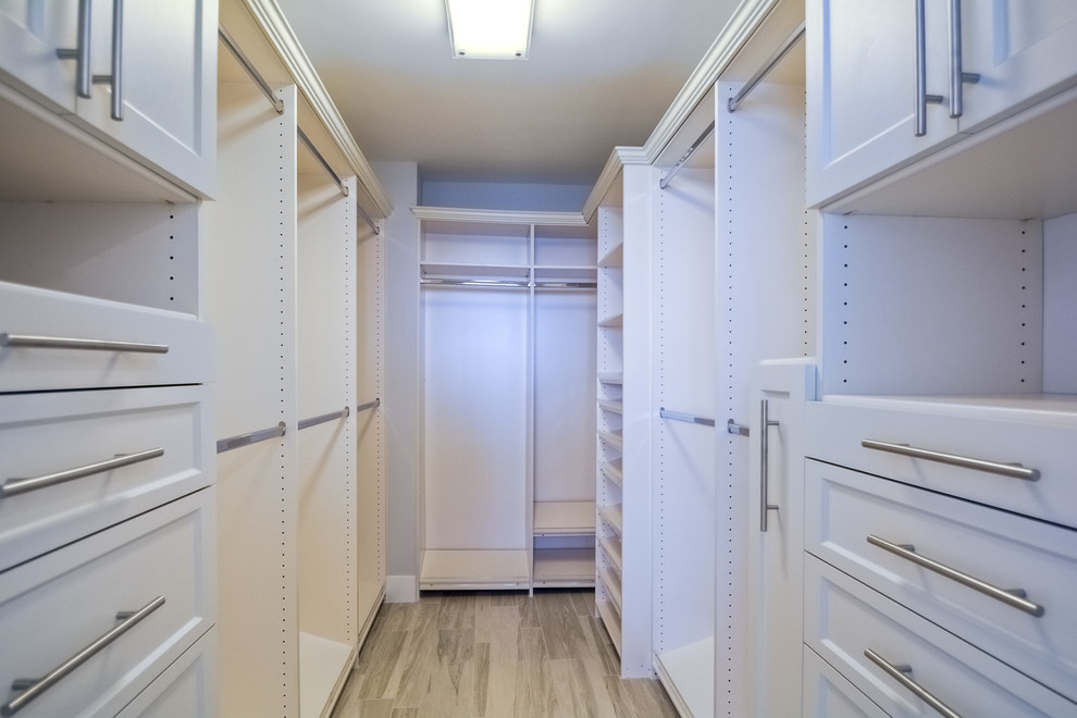 This is an example of a small coastal gender neutral walk-in wardrobe in San Diego with white cabinets, light hardwood flooring and recessed-panel cabinets.